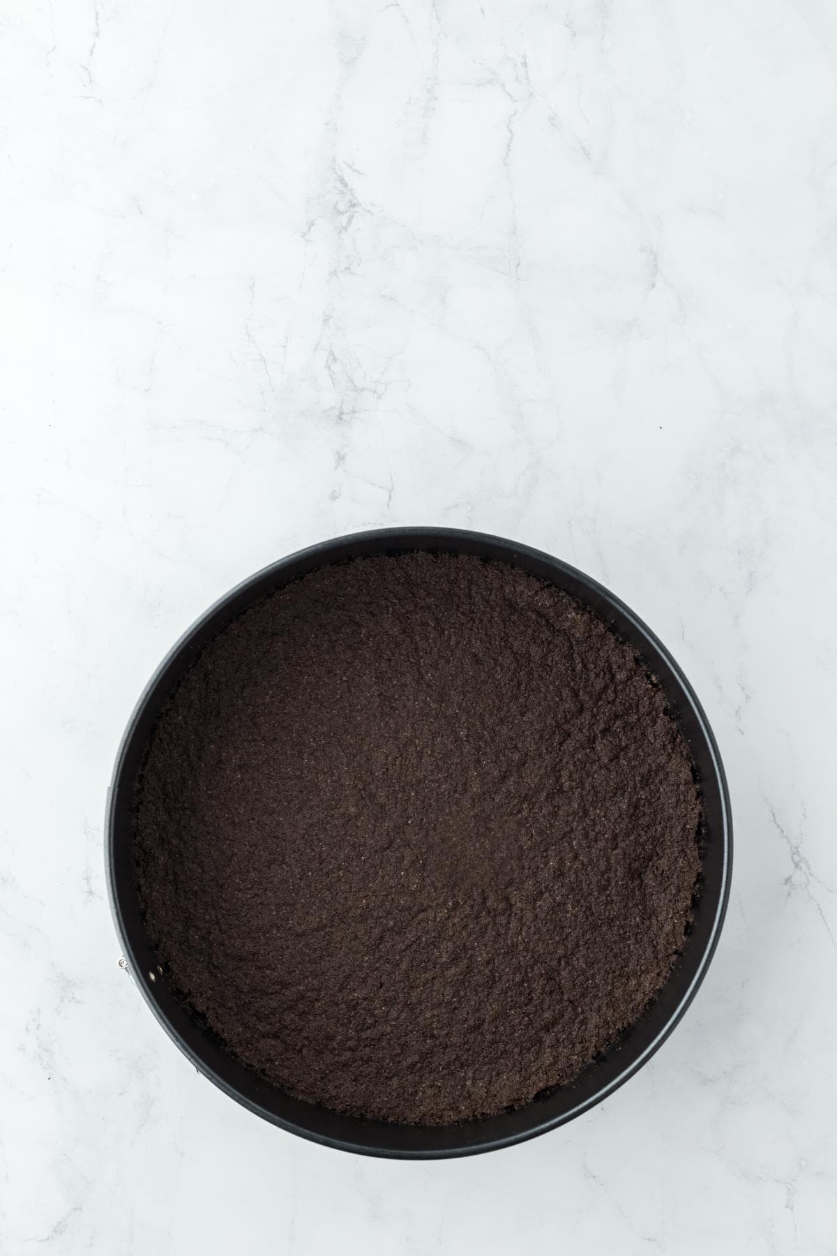 A springform pan with the oreo crust mixture pressed evenly into the bottom