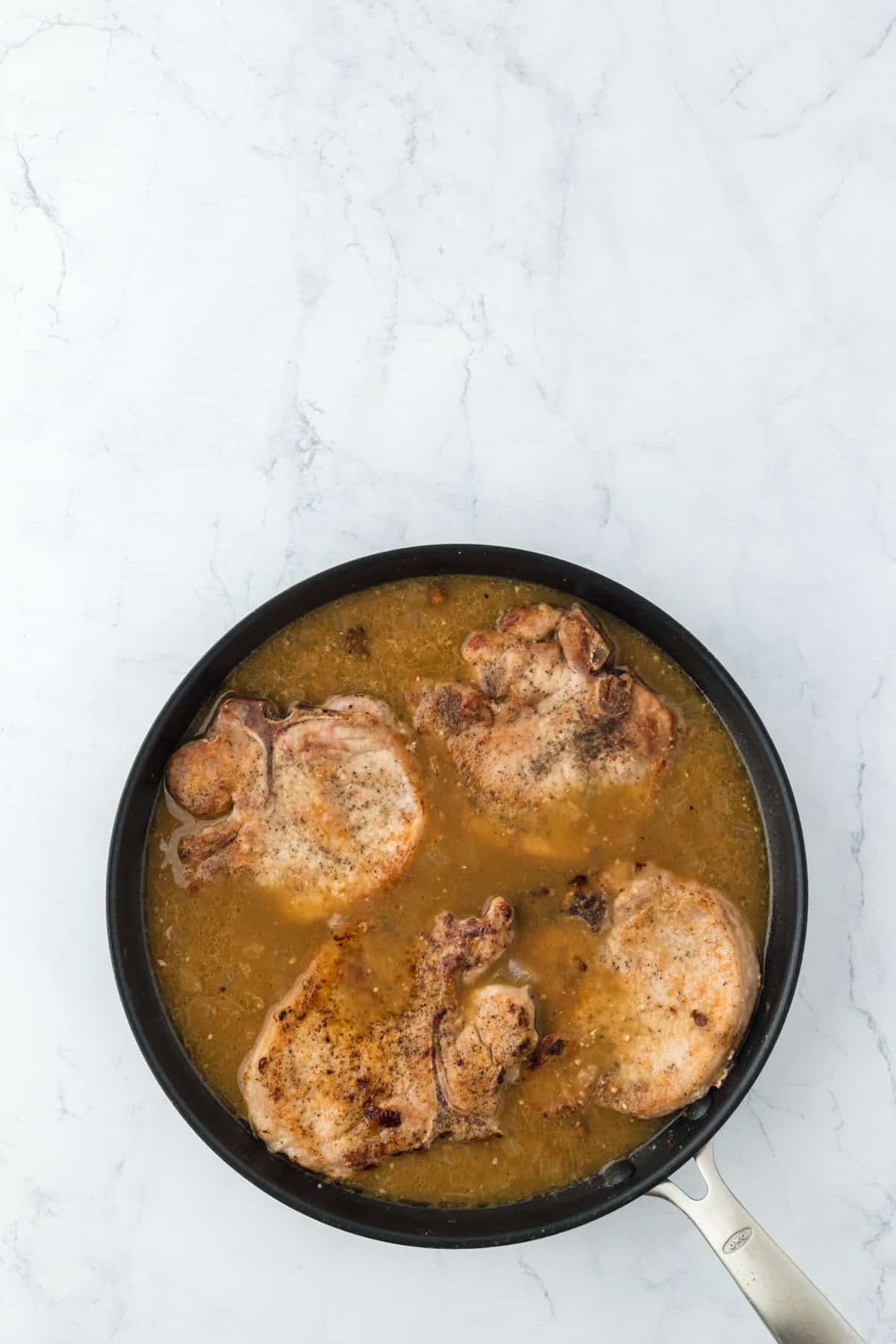 Breaded pork chops added to a gravy in skillet