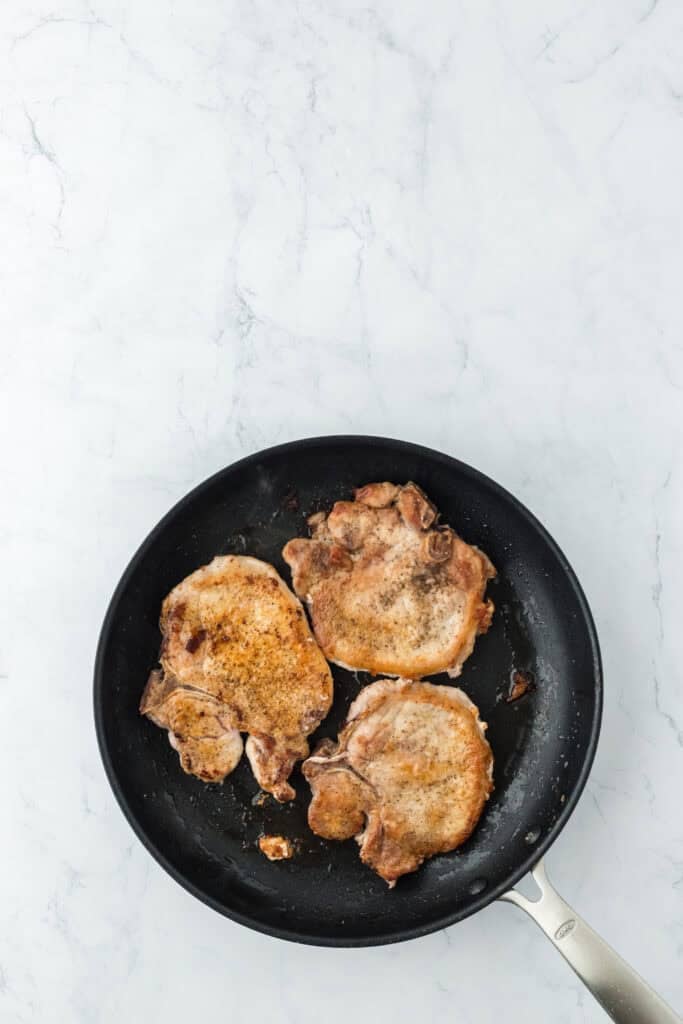 Fried pork chops in skillet being browned