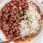 A white bowl of red beans and rice ready to enjoy against white background and white striped napkin