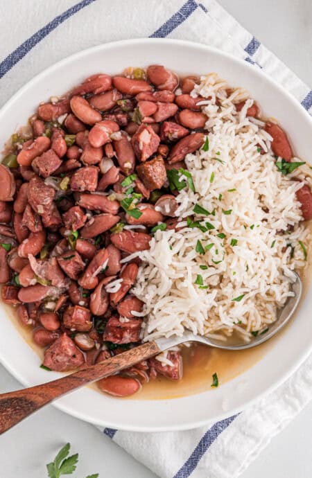 A white bowl of red beans and rice ready to enjoy against white background and white striped napkin