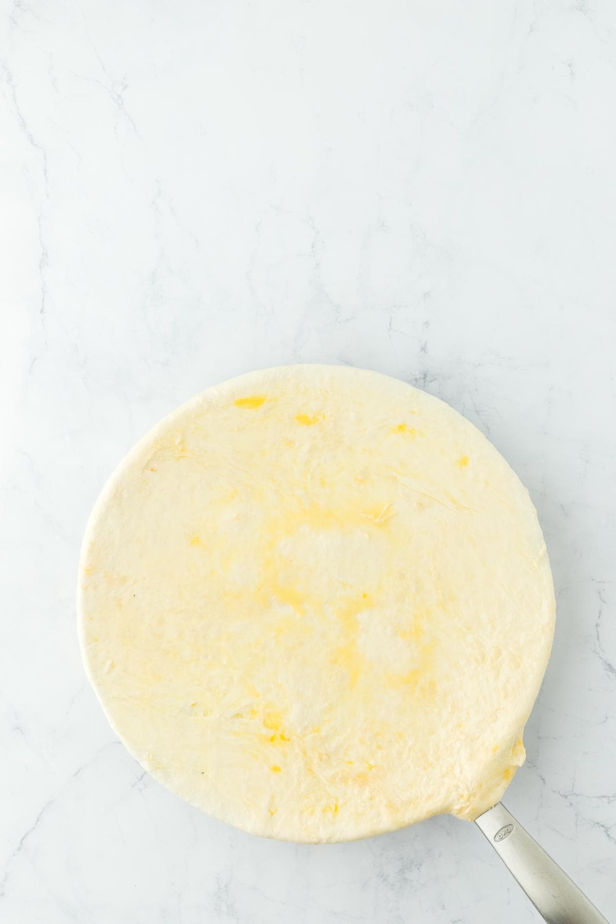 A round, uncooked pie crust, lightly brushed with egg wash or butter, placed over a black frying pan, on a white marble surface