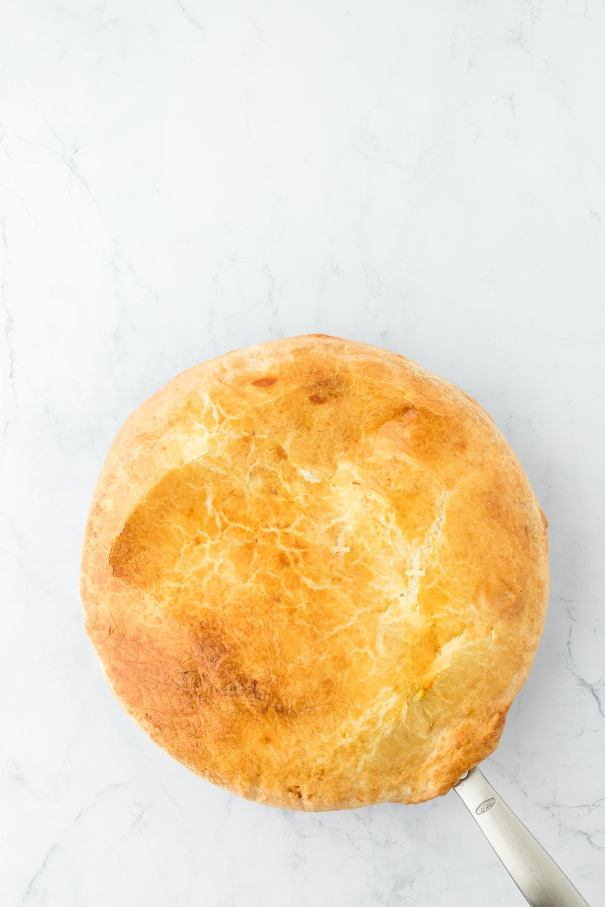A golden-brown, baked pie crust covering a round pan, seen from above on a white marble surface