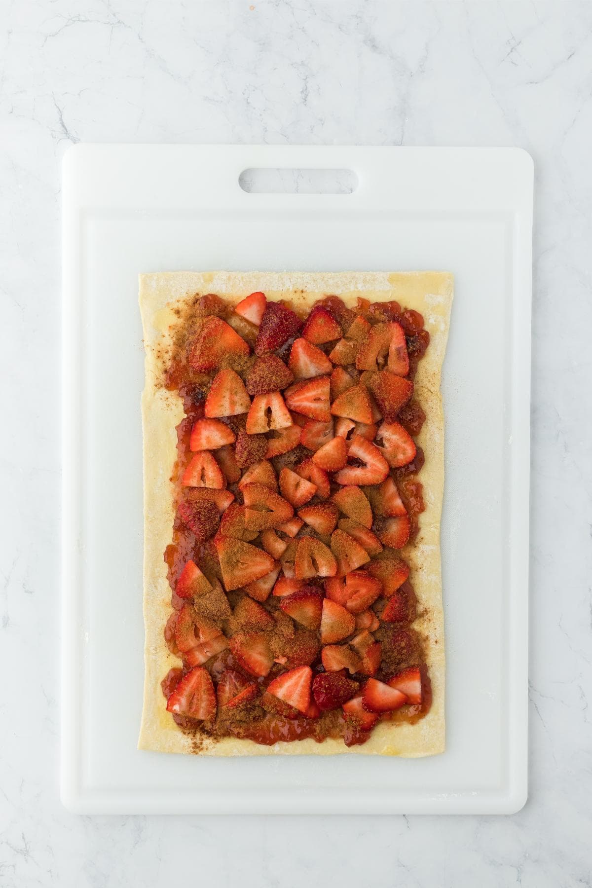 Layer of strawberry jam and sliced strawberries spread on a rolled-out rectangle of dough
