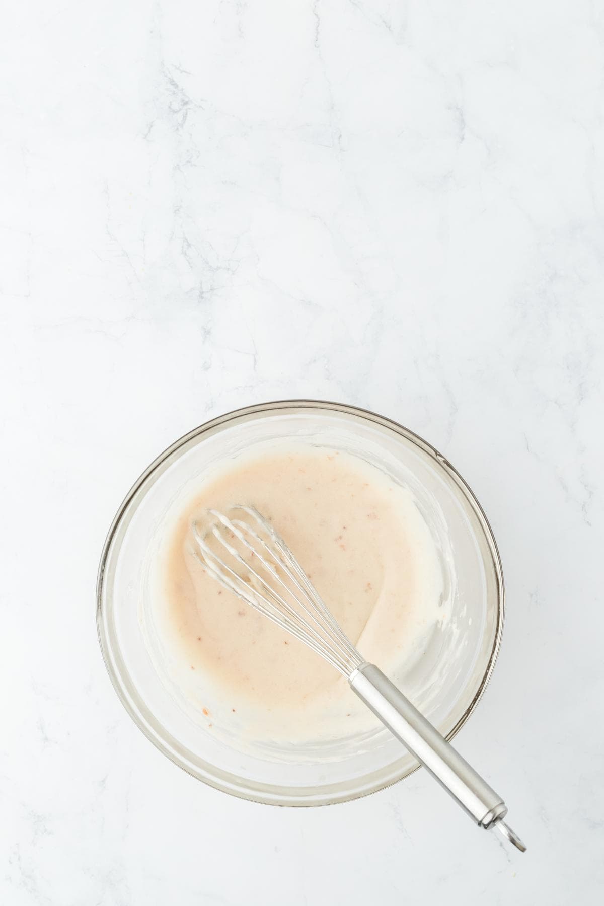 A clear bowl containing the mixed glaze with a whisk in it
