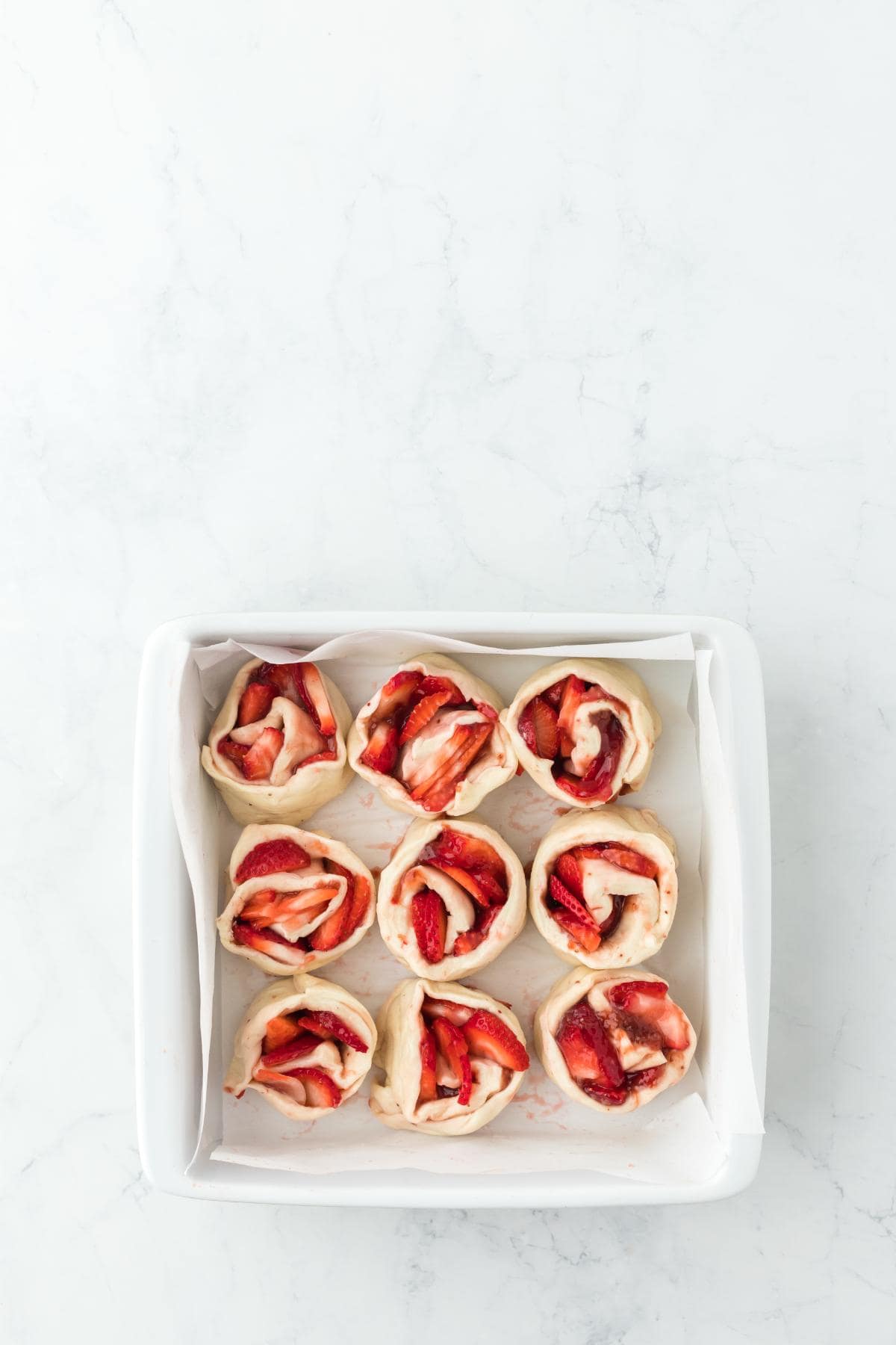 Strawberry cinnamon rolls arranged in a greased baking dish before baking