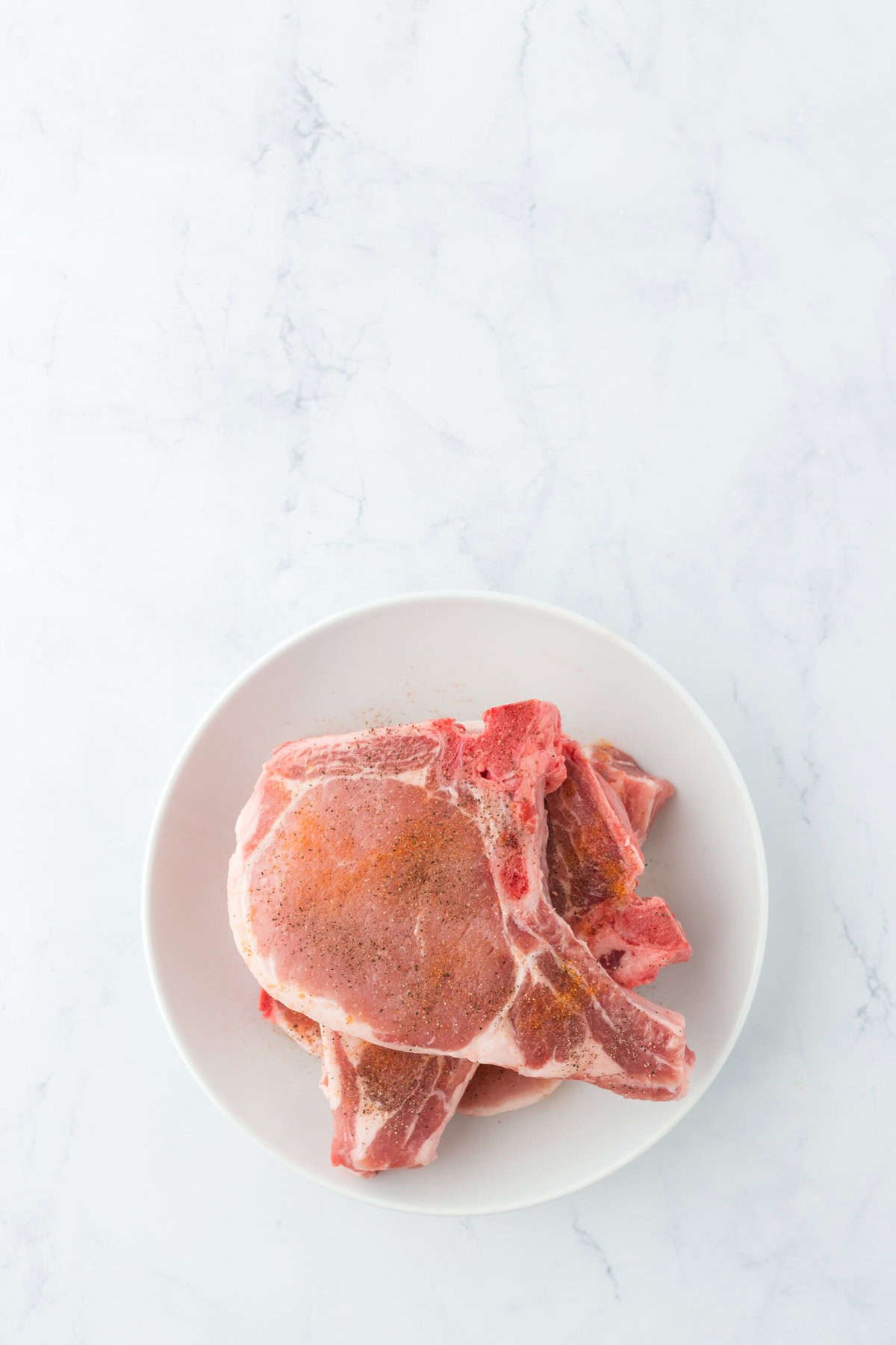 Pork chops on a white plate with seasoned salt on it on countertop