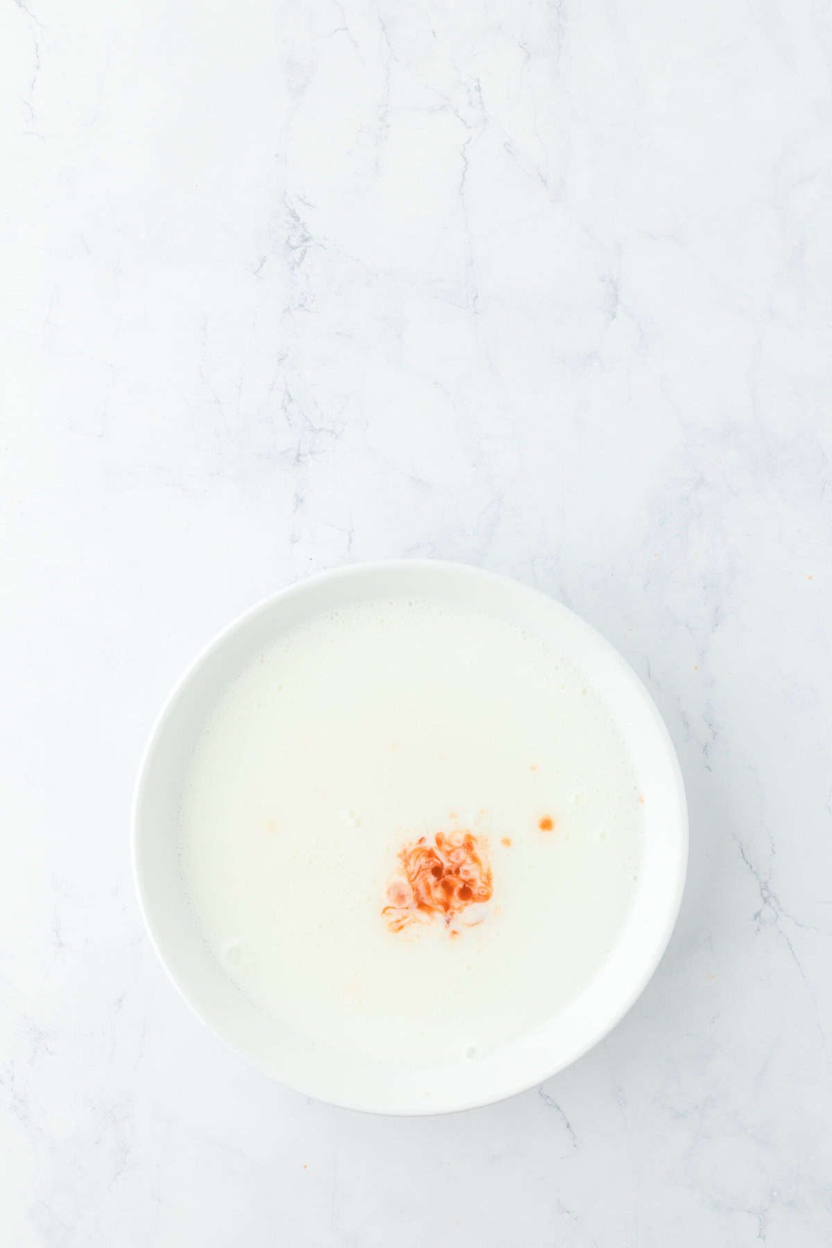 Buttermilk with hot sauce in a white bowl on white countertop