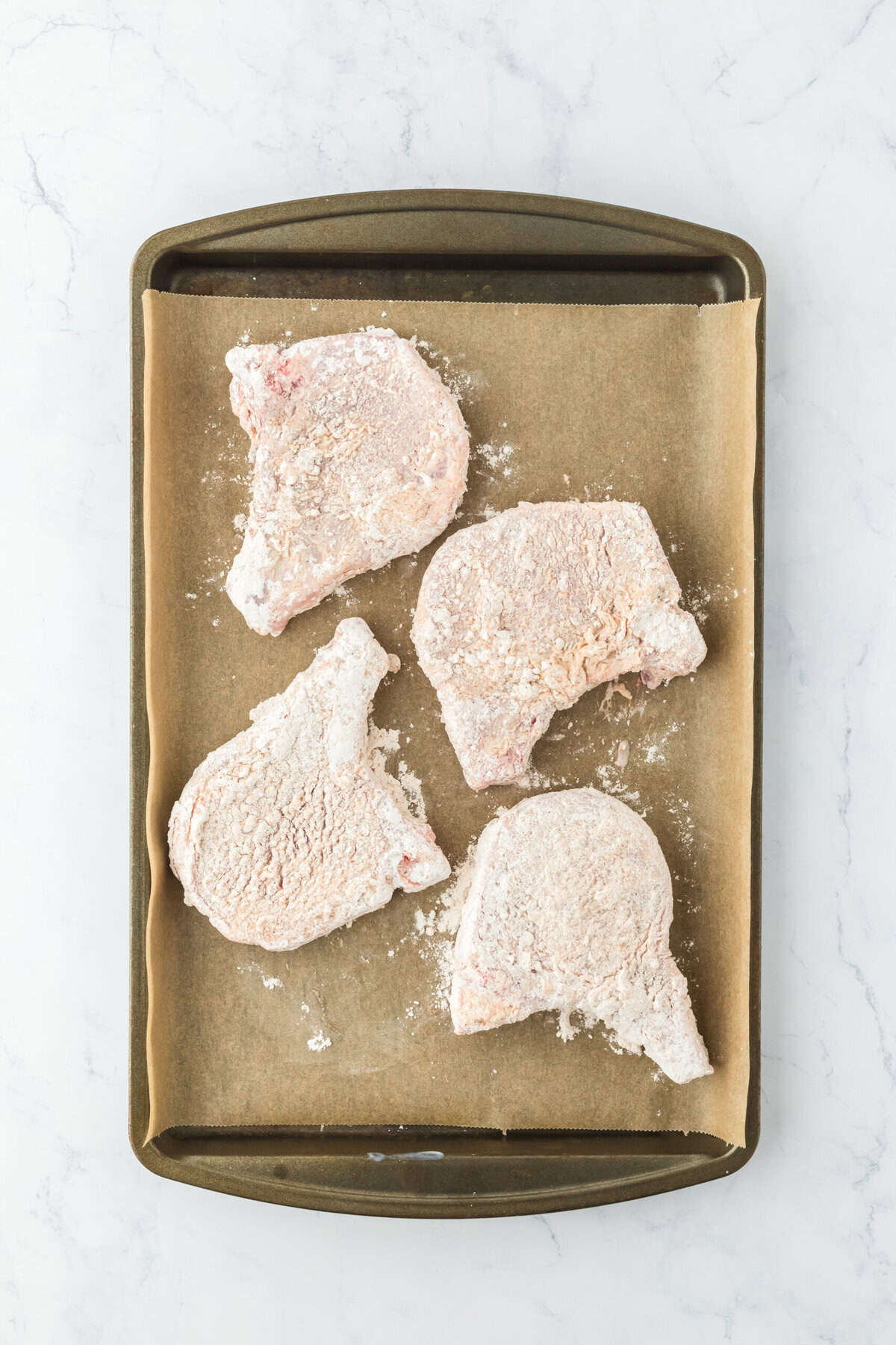 Dredged pork chops on parchment lined baking sheet