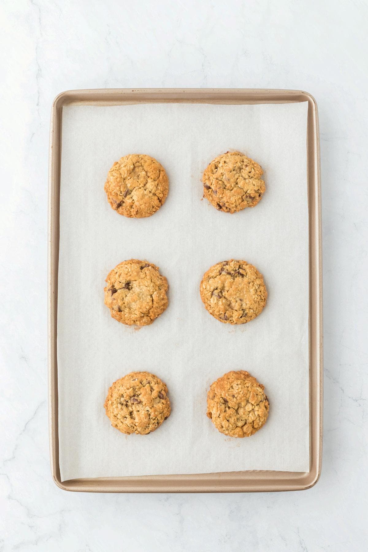 Freshly baked oatmeal chocolate chip cookies on a parchment-lined baking sheet