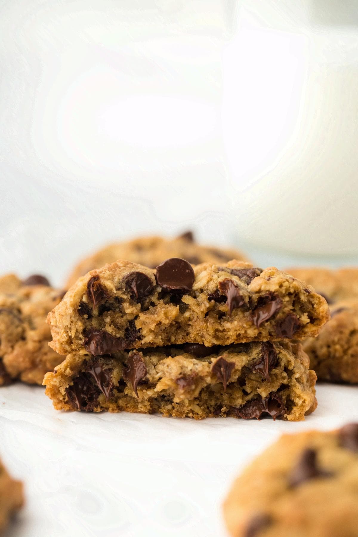 Stacked oatmeal chocolate chip cookies broken in half, showing soft, melted chocolate chips in the center