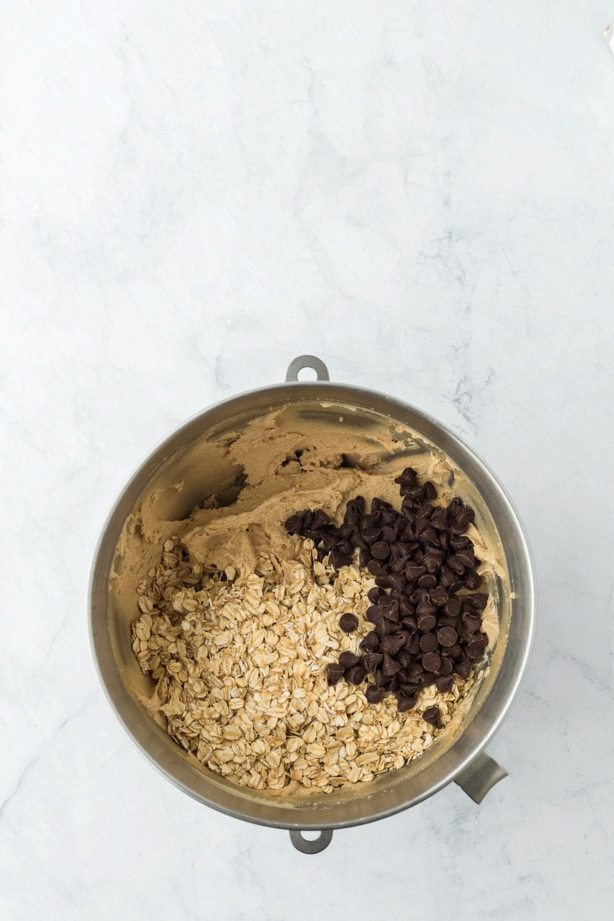 Oats and chocolate chips added to cookie dough in a mixing bowl
