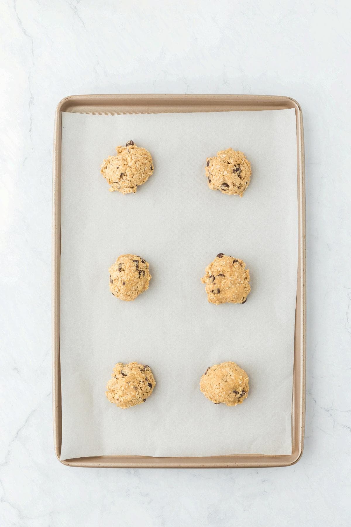 Portioned oatmeal chocolate chip cookie dough balls on a parchment-lined baking sheet