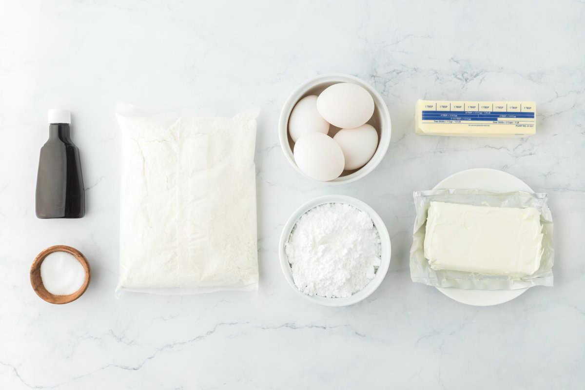 Ingredients of cake mix, eggs, butter, cream cheese, sugar, vanilla on a white background