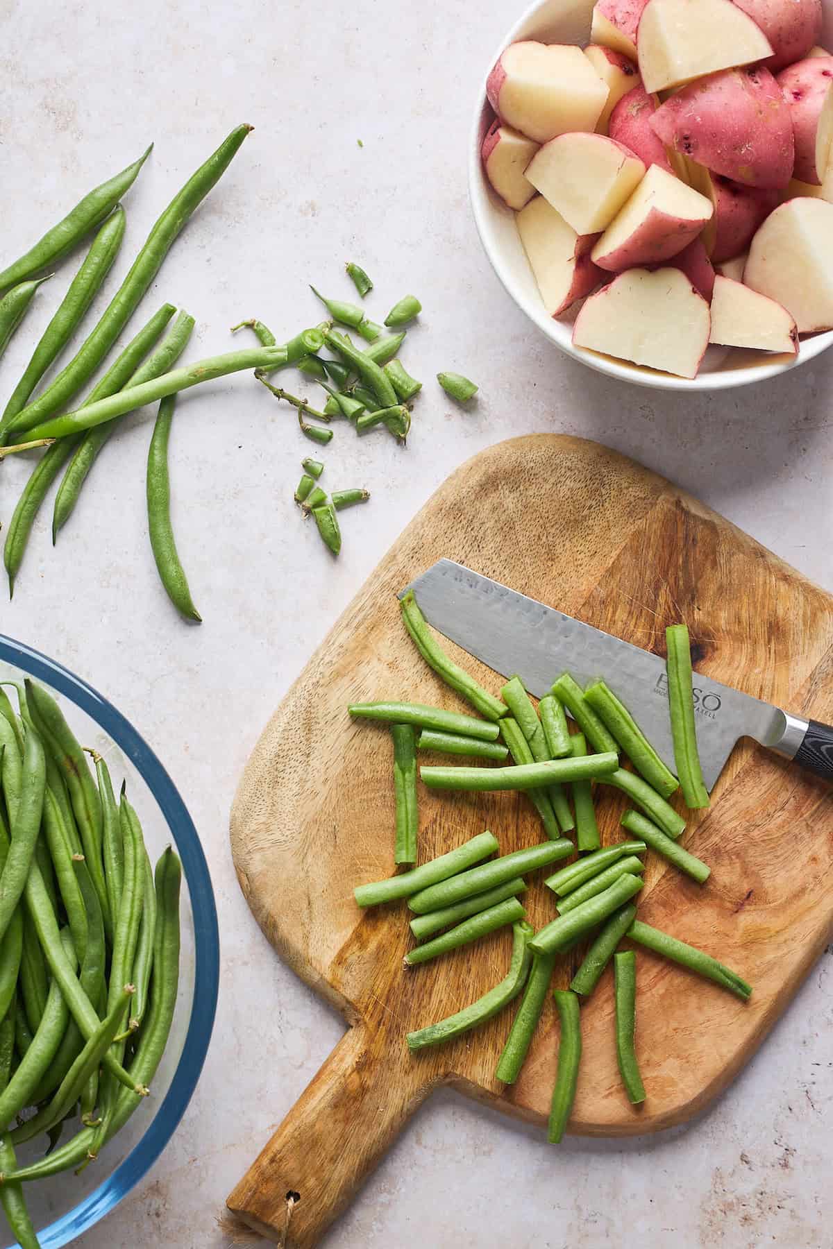 Green beans cut and stemmed in a bowl and potatoes in a bowl nearby on a cutting board