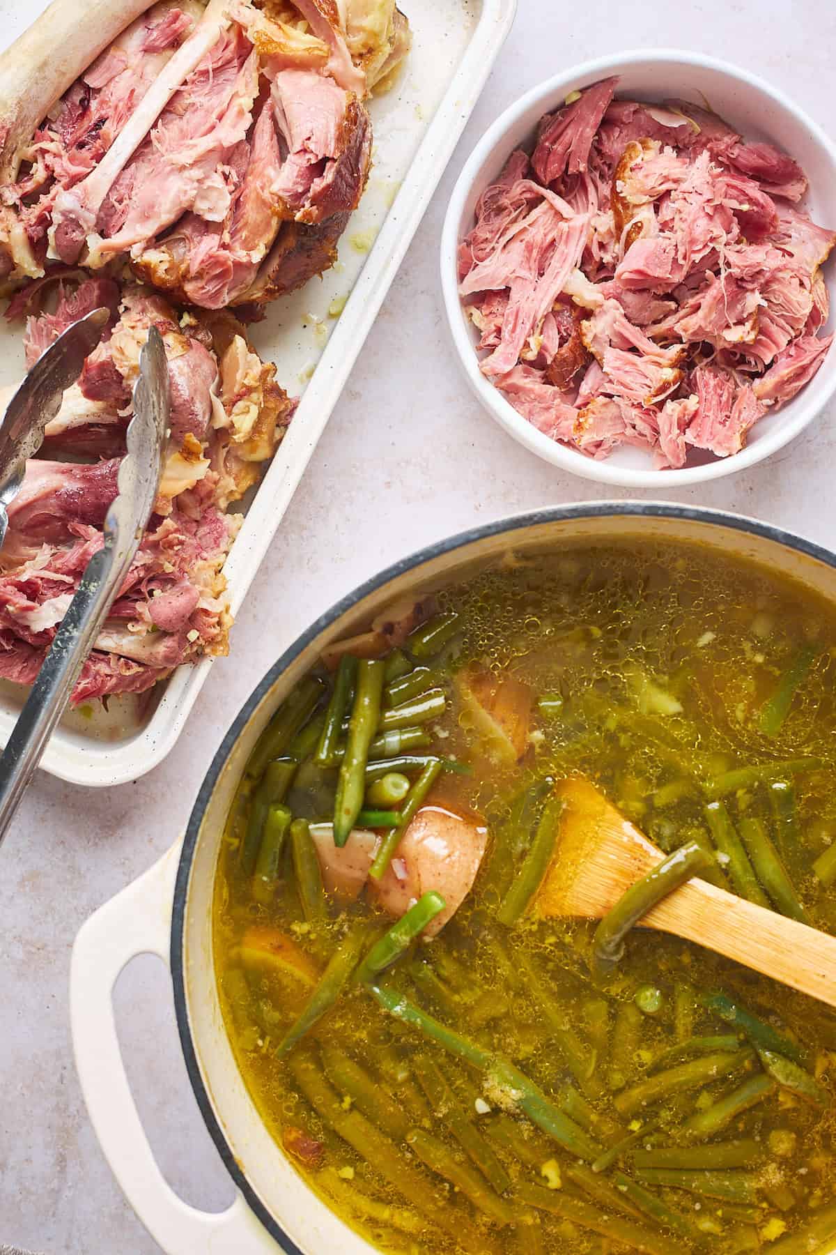 Smoked turkey being removed from pot of green beans and being shredded