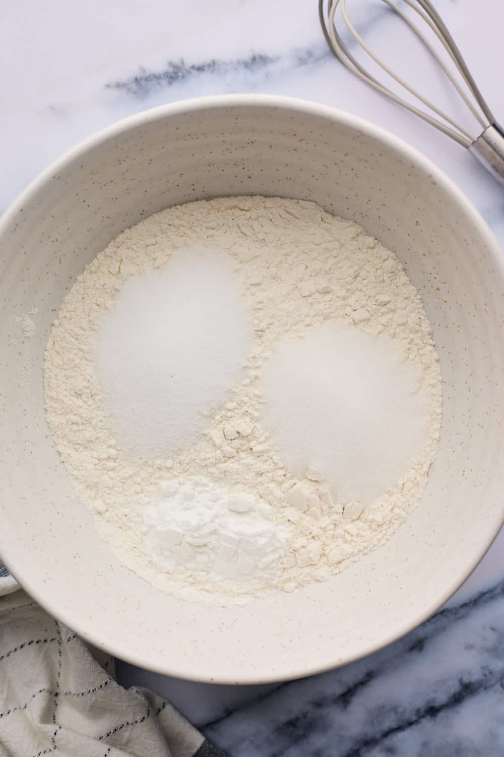 Flour along with dry ingredients in a white bowl on white background with whisk