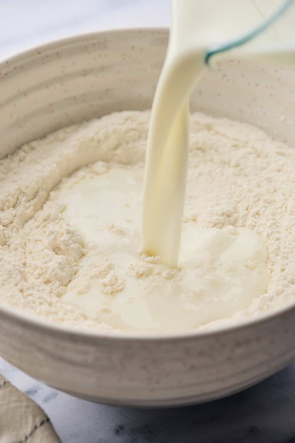 Buttermilk being added to dry mixture of ingredients in a large mixing bowl