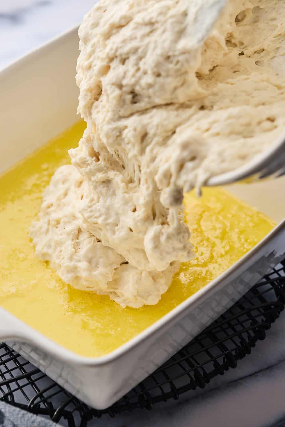 Butter swim biscuit dough being added to melted butter in a baking dish on white background