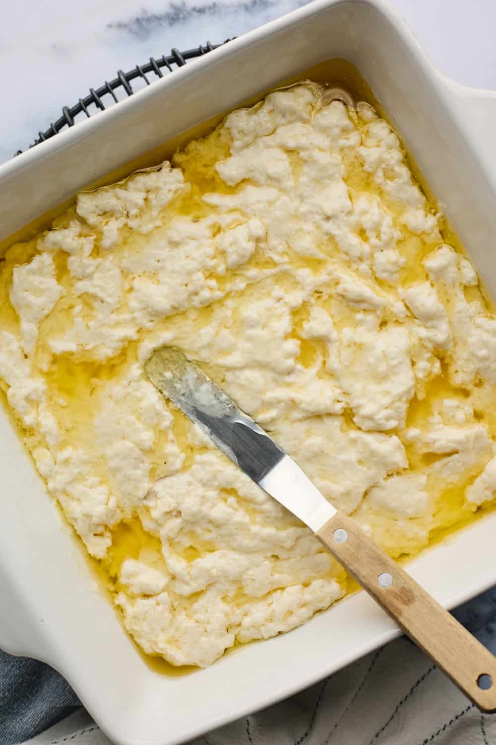 Biscuit dough being spread with a spatula in baking dish on white background