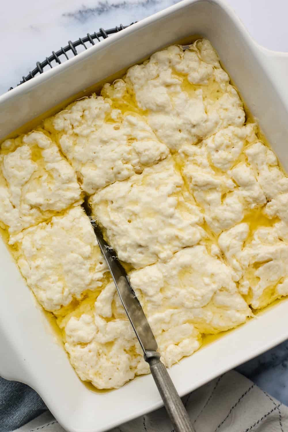 A butter knife cutting through butterswim biscuits before baking on white background