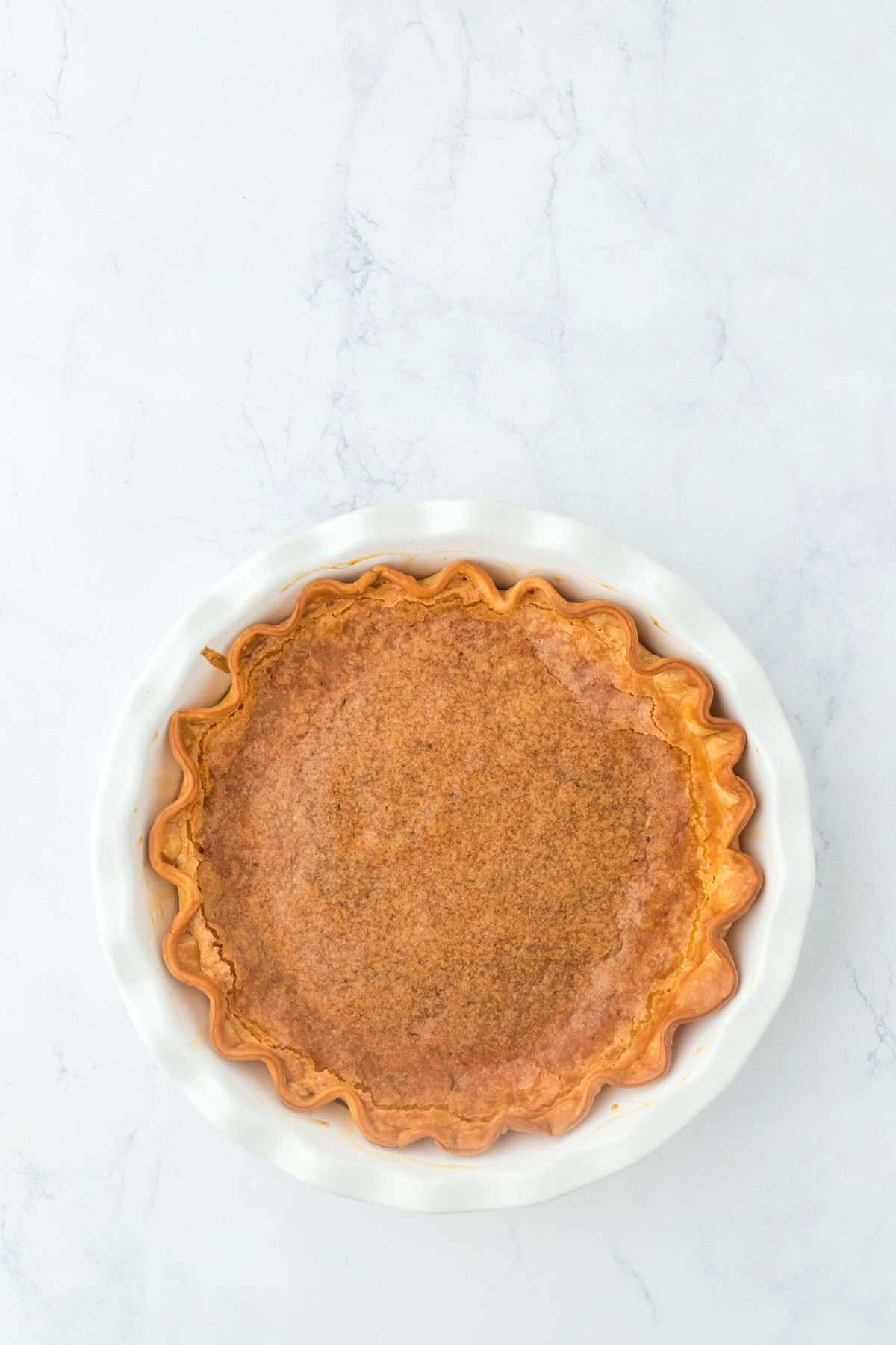 A chess pie out of the oven browned and cooling on a white background