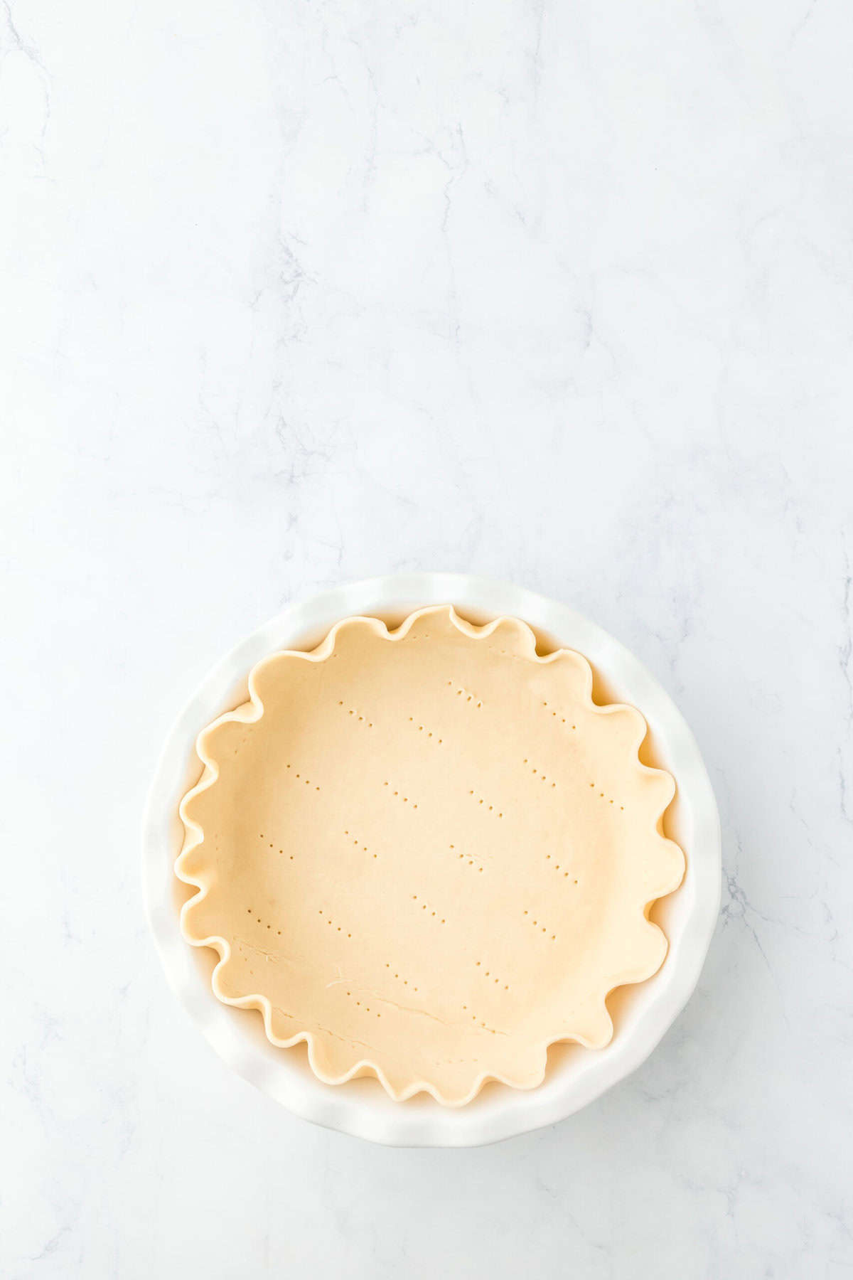 Pie dough crimped in a pie plate on a white background