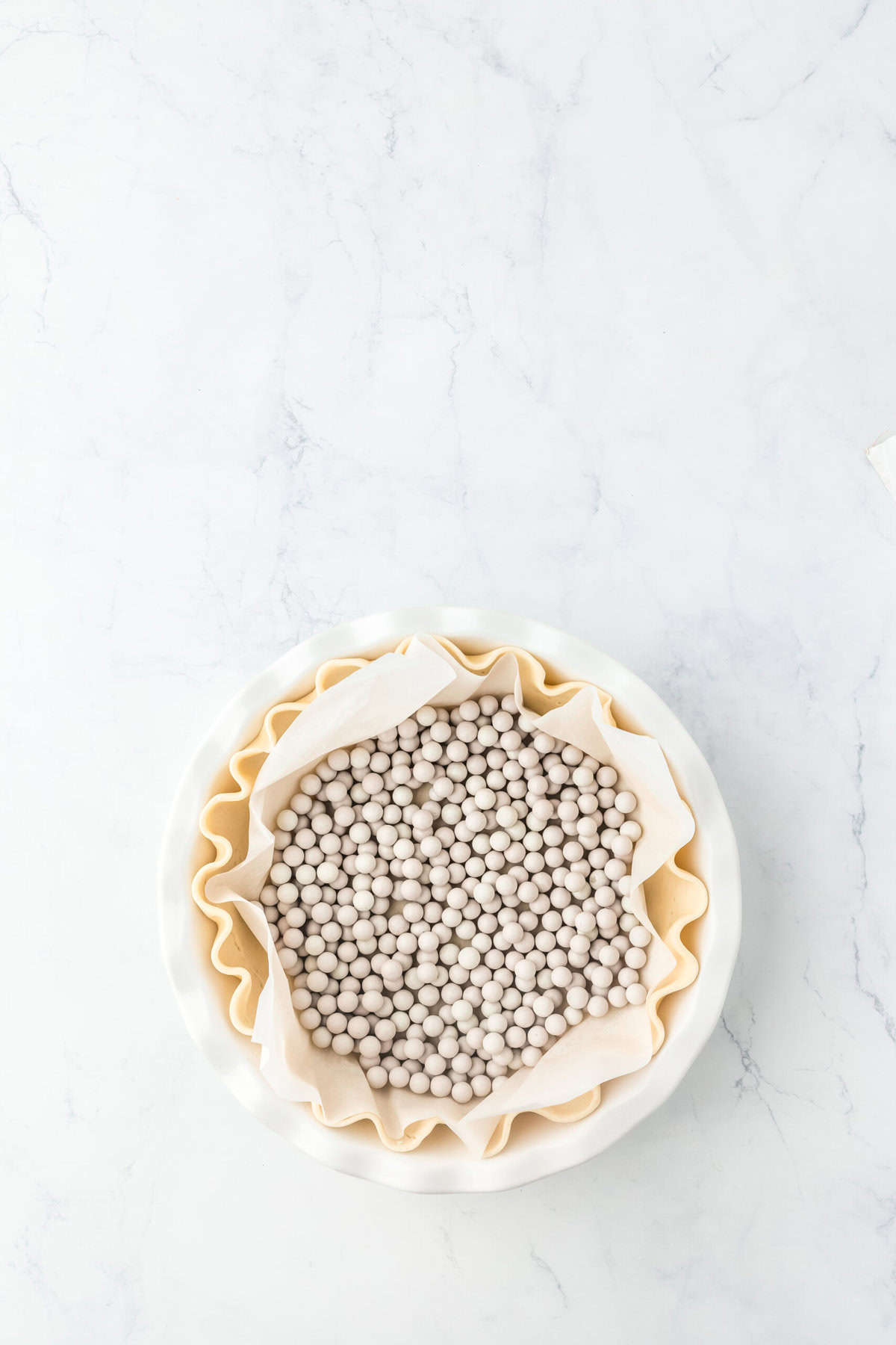 Pie dough added to a pie plate with pie weights on parchment on white background