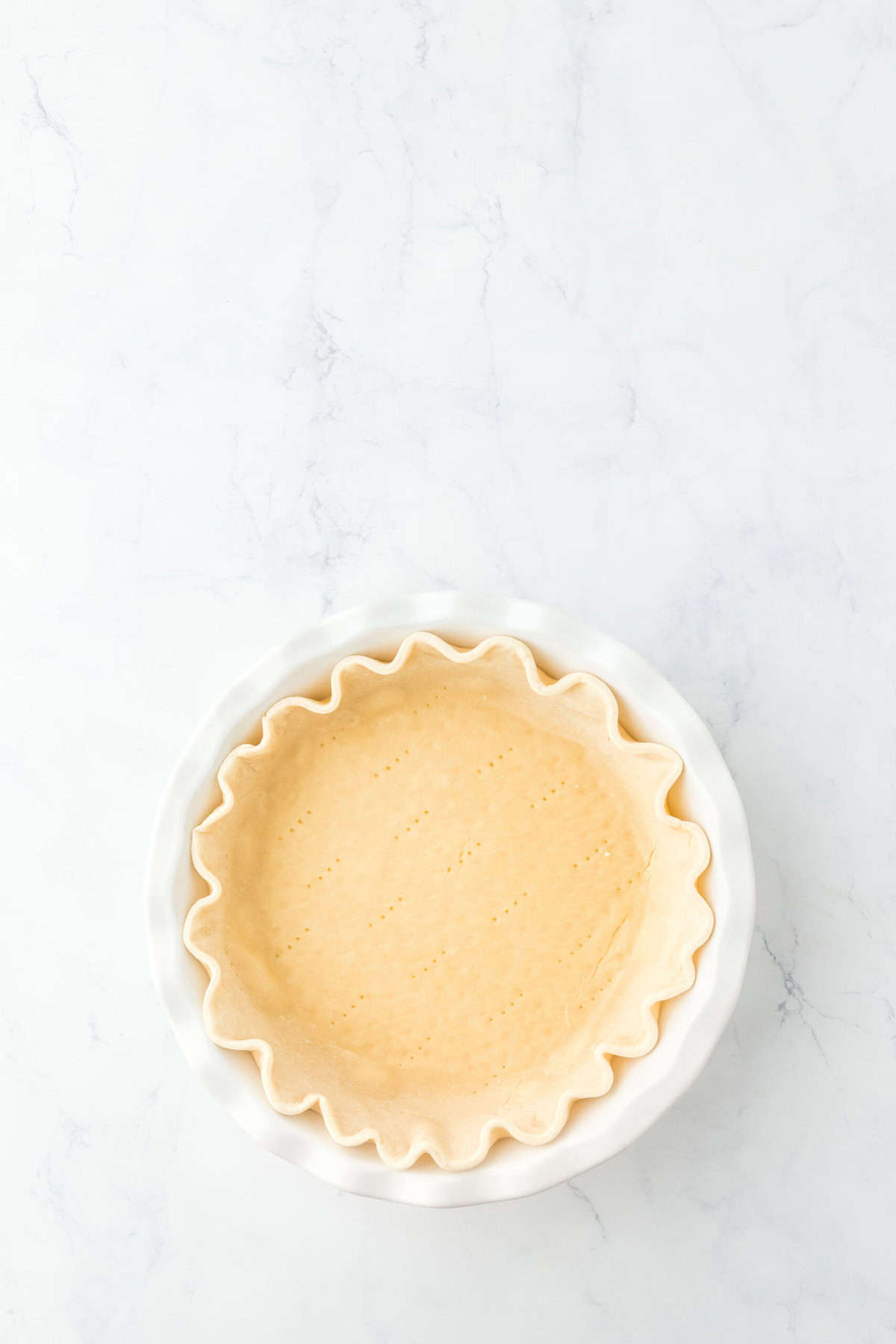 Blind baked pie dough in a white pie plate on white background