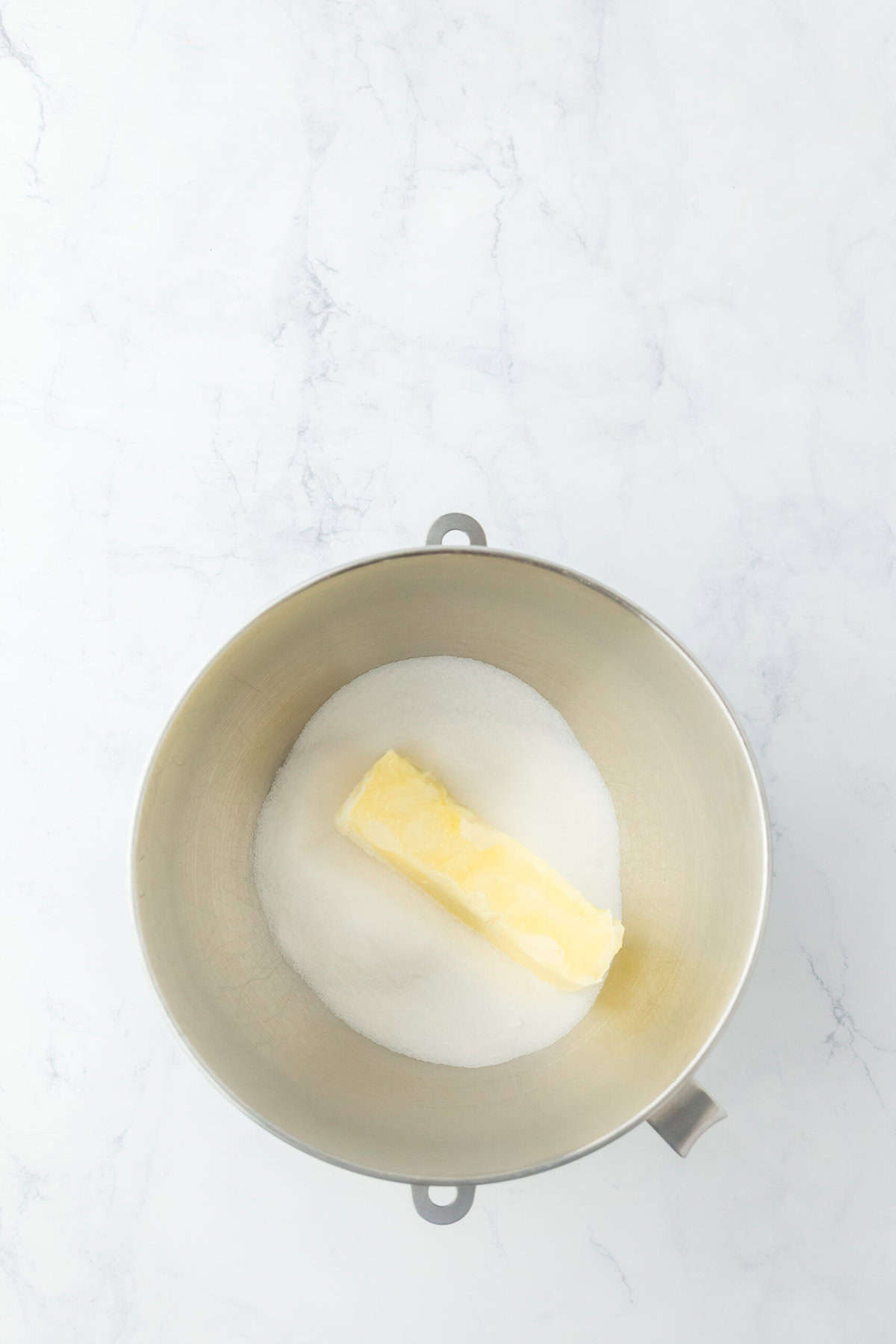 Butter and granulated sugar added to a stand mixer on a white background