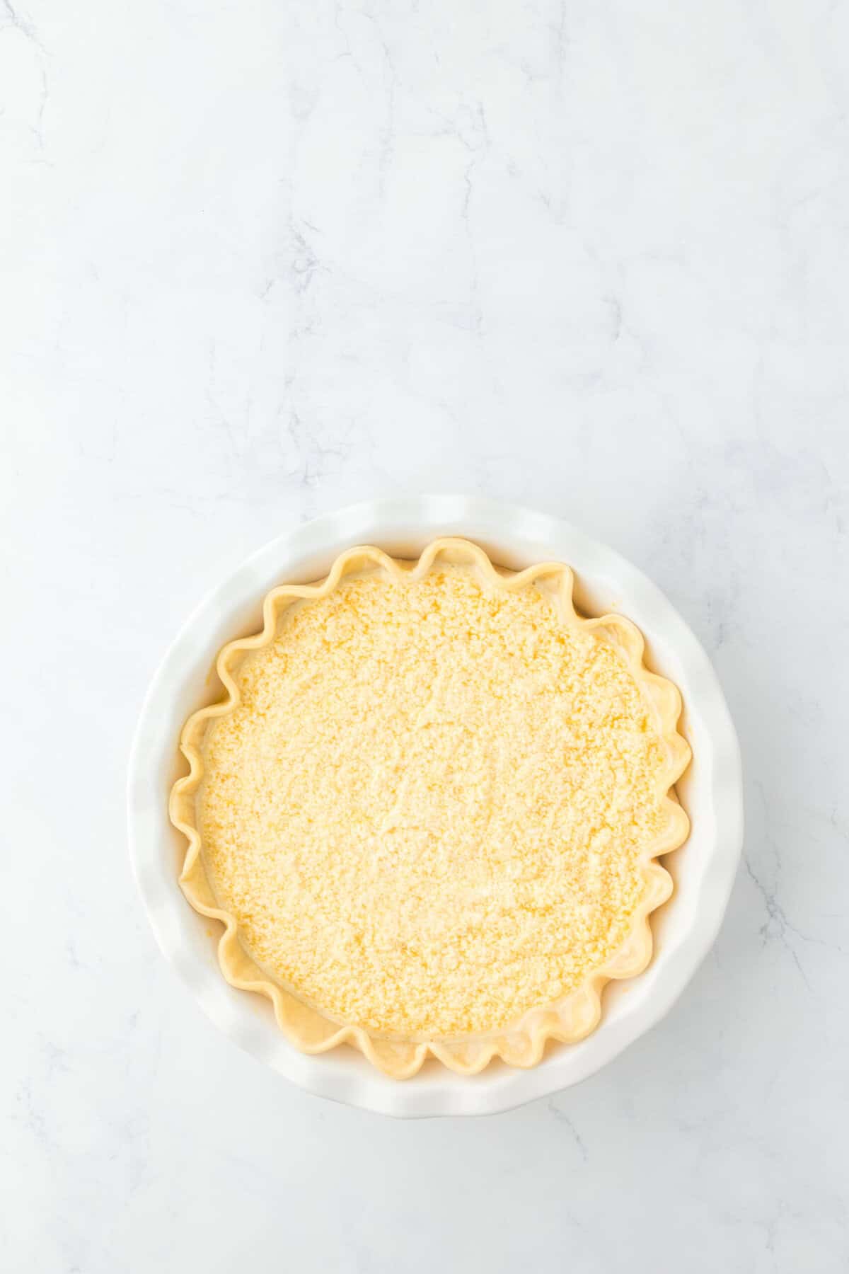 Pie filling added to a blind baked pie crust on a white background