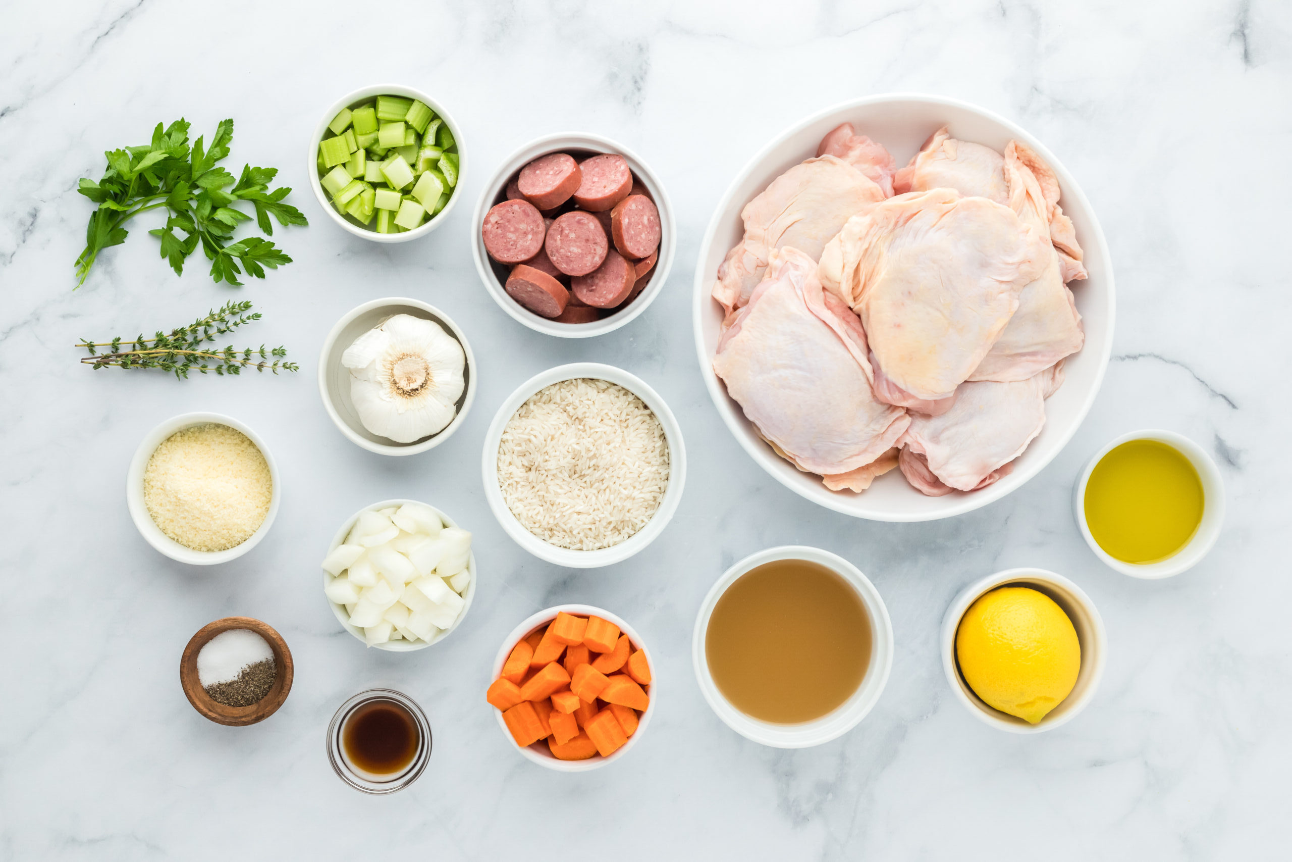 Chicken pieces, sausage, veggies, spices and herbs in white bowls on white background