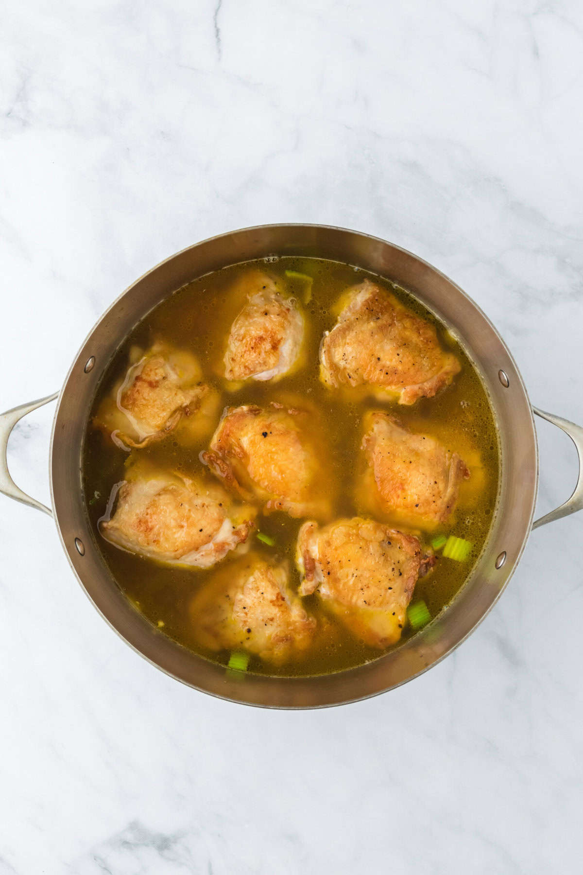 Chicken added in a large pot with broth on a white background