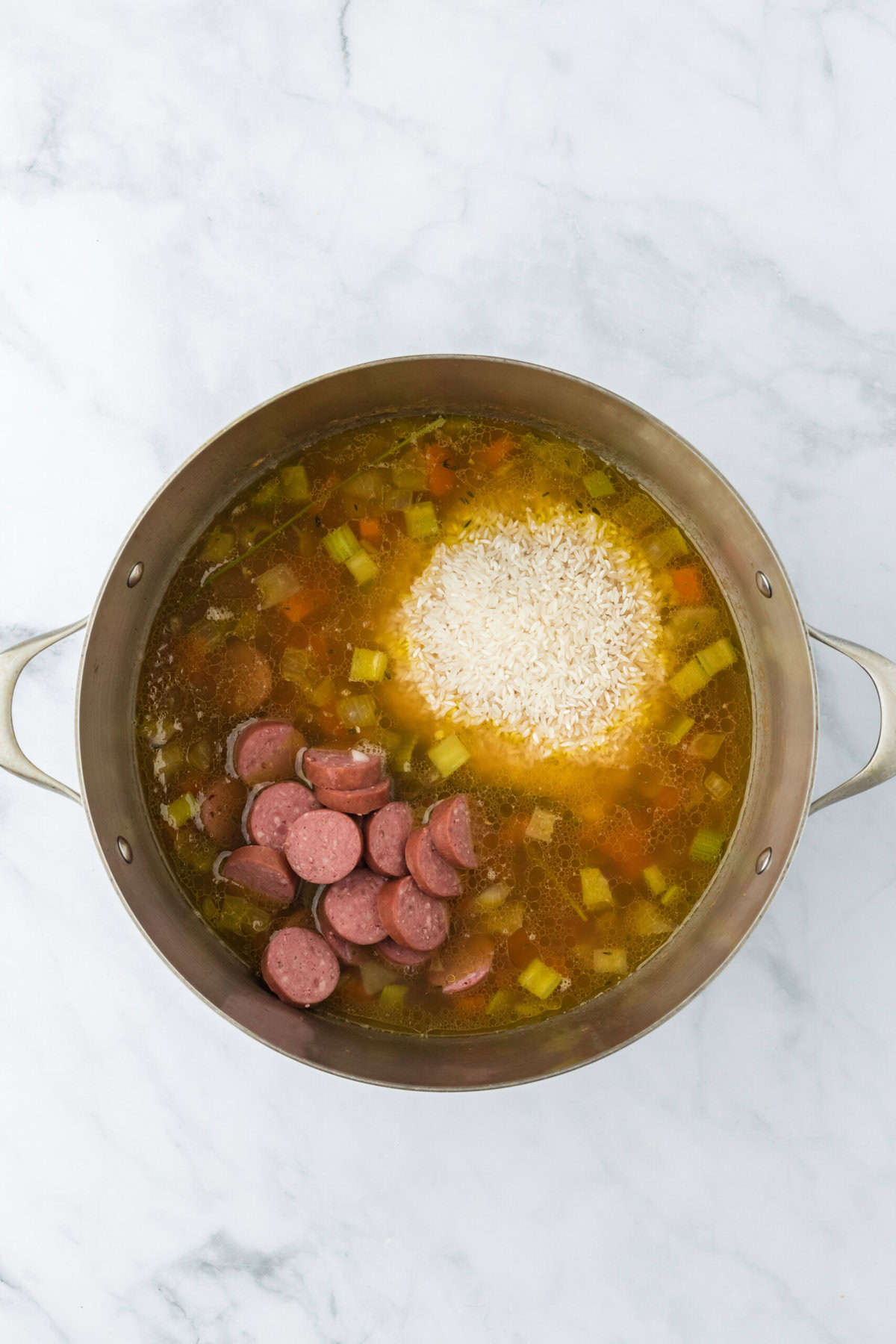 Sausage and rice added to a large dutch oven on a white background