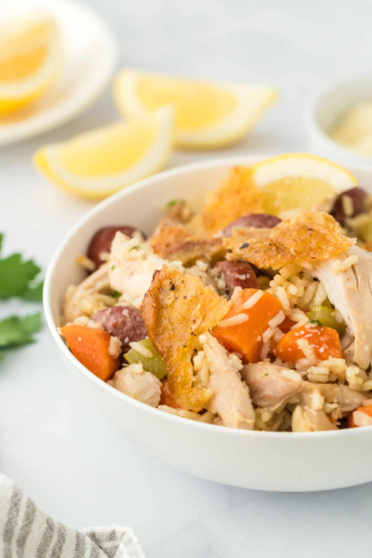 A large white bowl with chicken bog recipe with lemon wedges in the white background