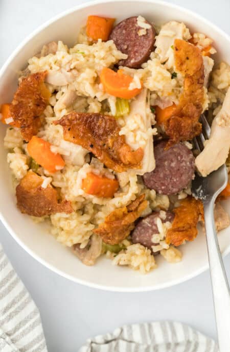 A large white bowl filled with chicken bog with a spoon digging in on a white background