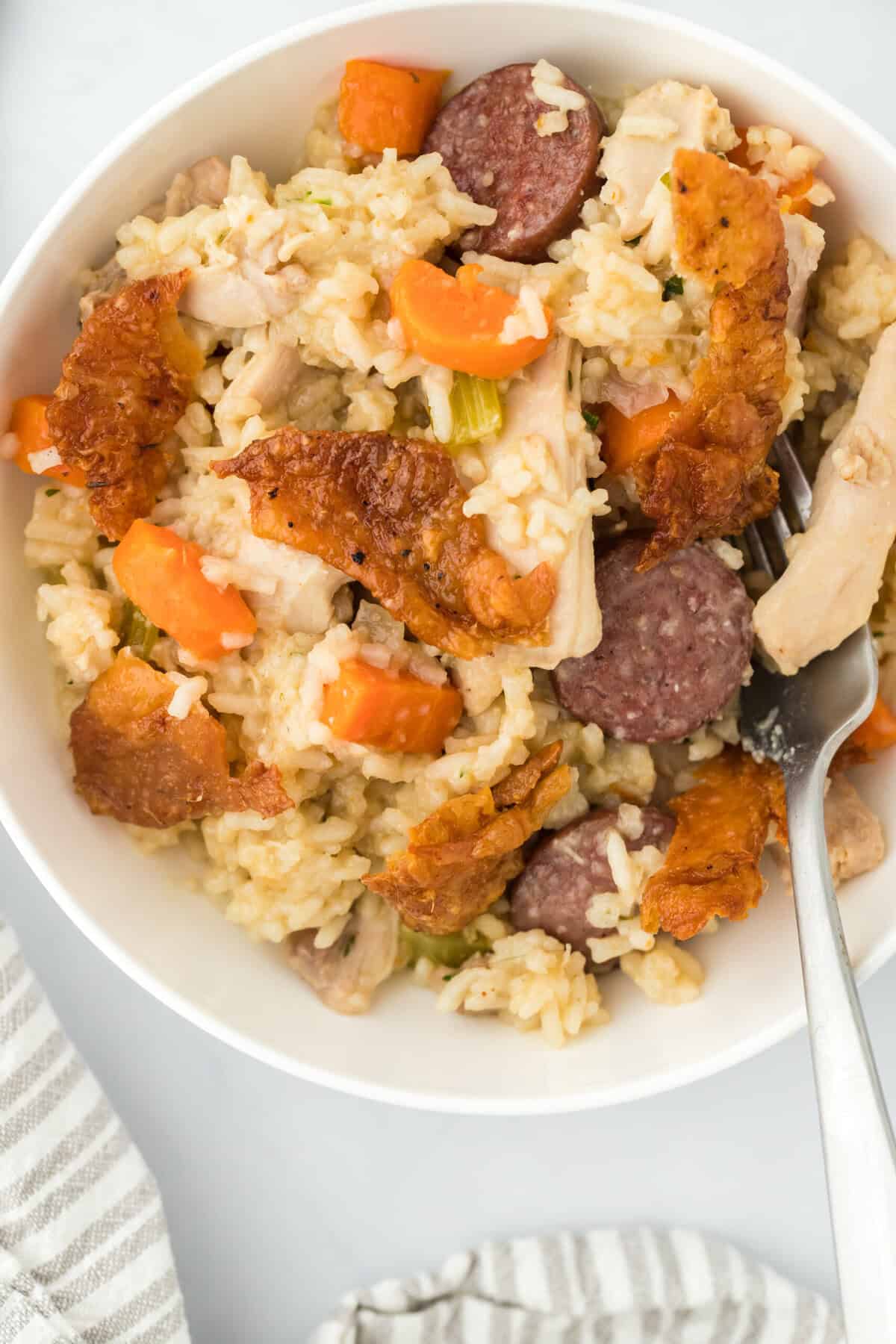 A large white bowl filled with chicken bog with a spoon digging in on a white background