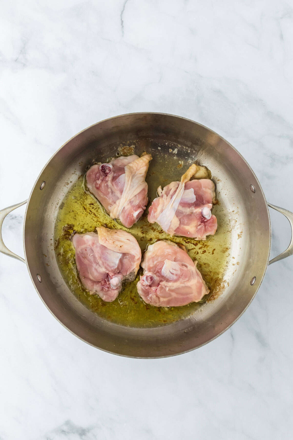 Chicken pieces being browned in olive oil in pot on white background