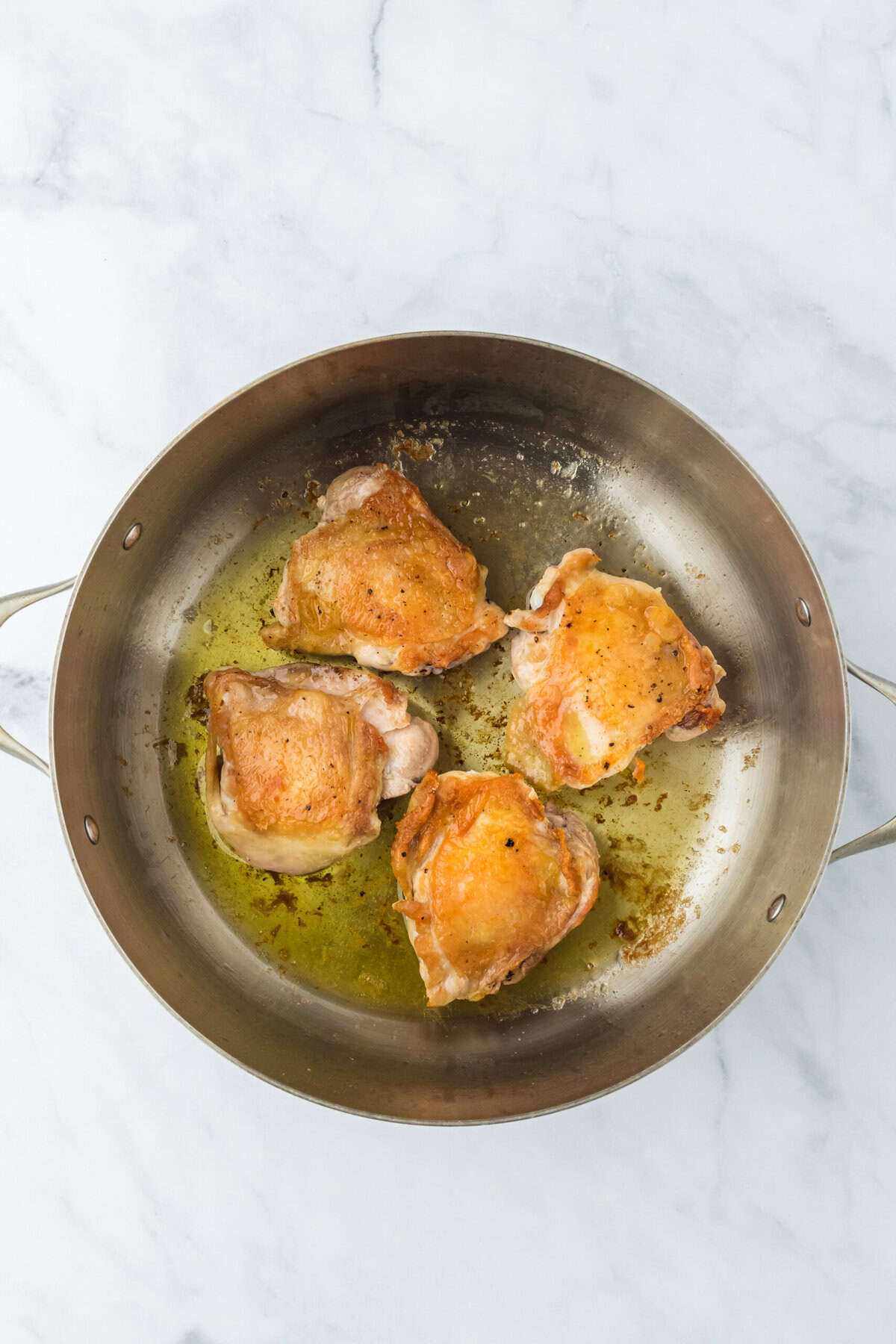 Browned chicken in a dutch oven that's on a white background