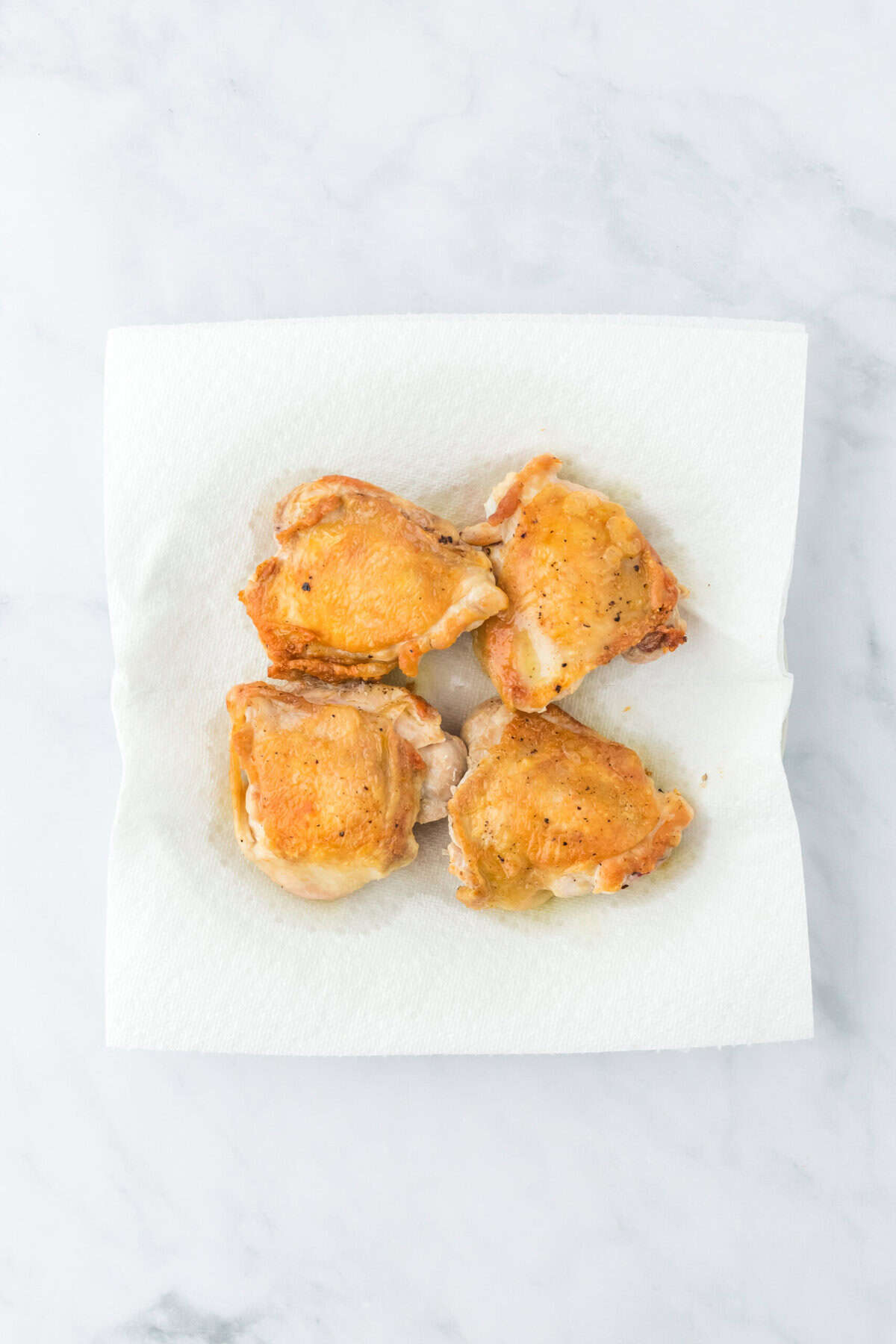 Drained chicken pieces on paper towels on white background