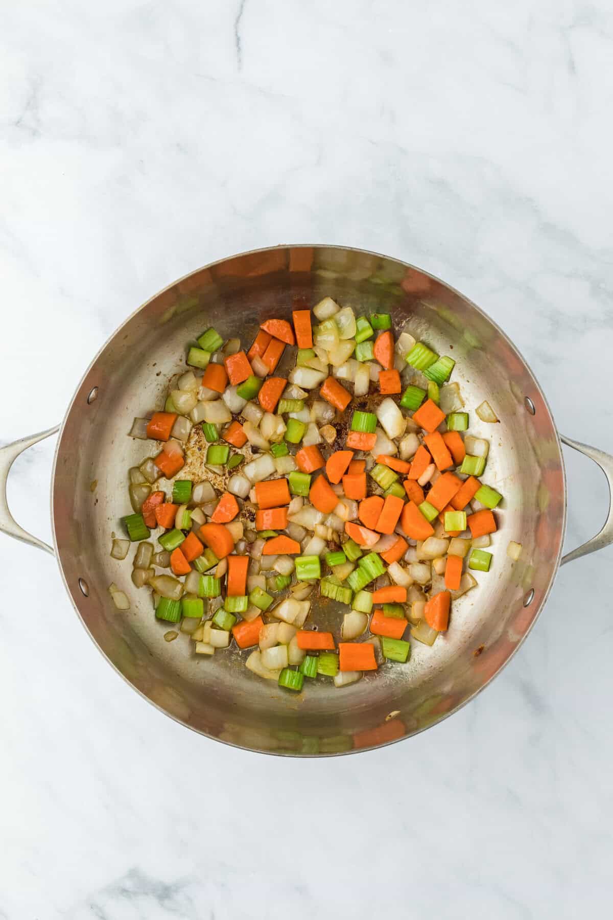 Celery, carrots, and onion cooked in a dutch oven with olive oil on a white background