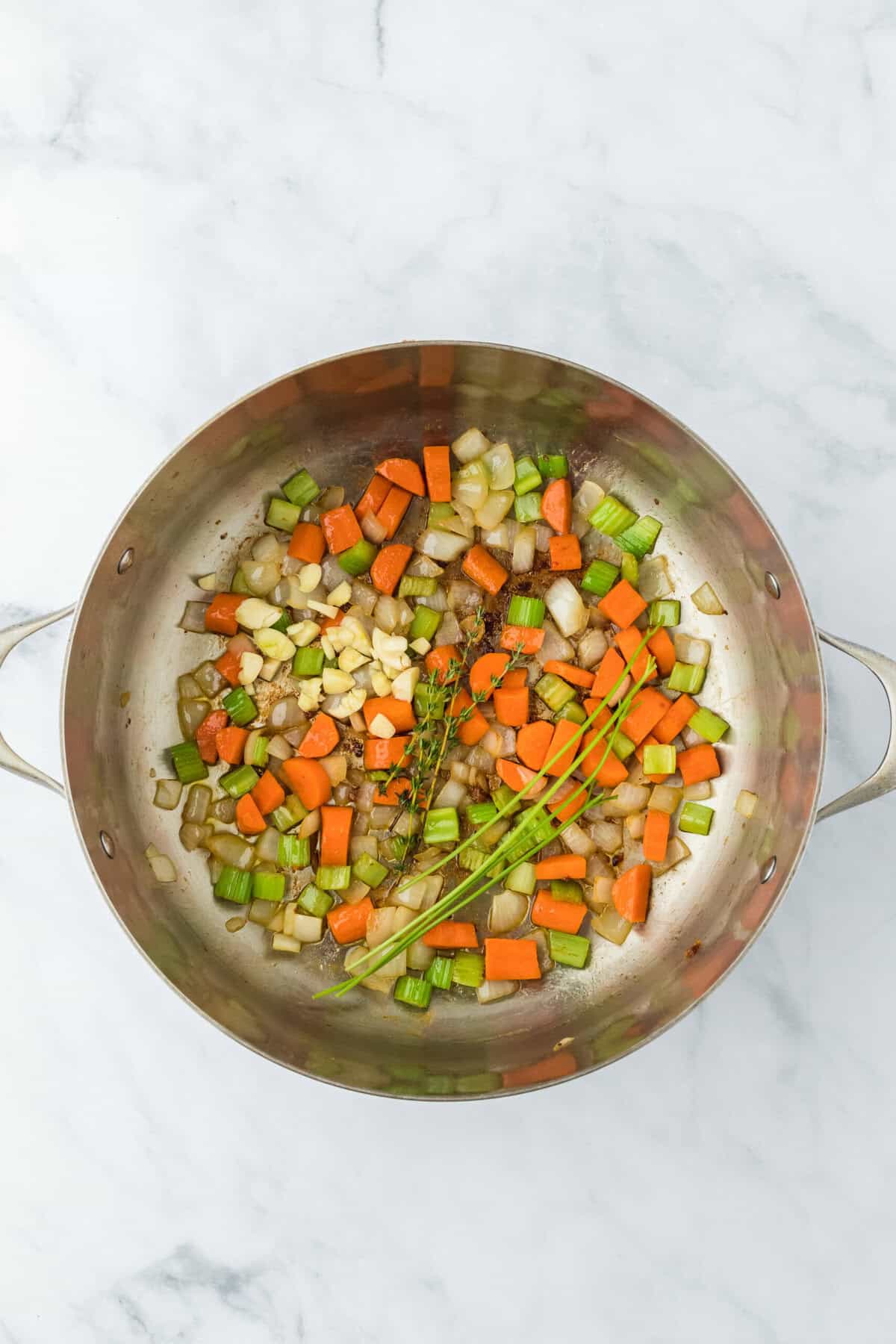 Thyme, garlic and parsley added to veggies in a pot on a white background