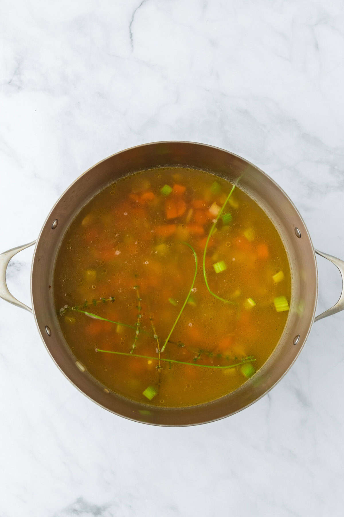 Chicken stock, water and worcestershire sauce added to a large pot on a white background