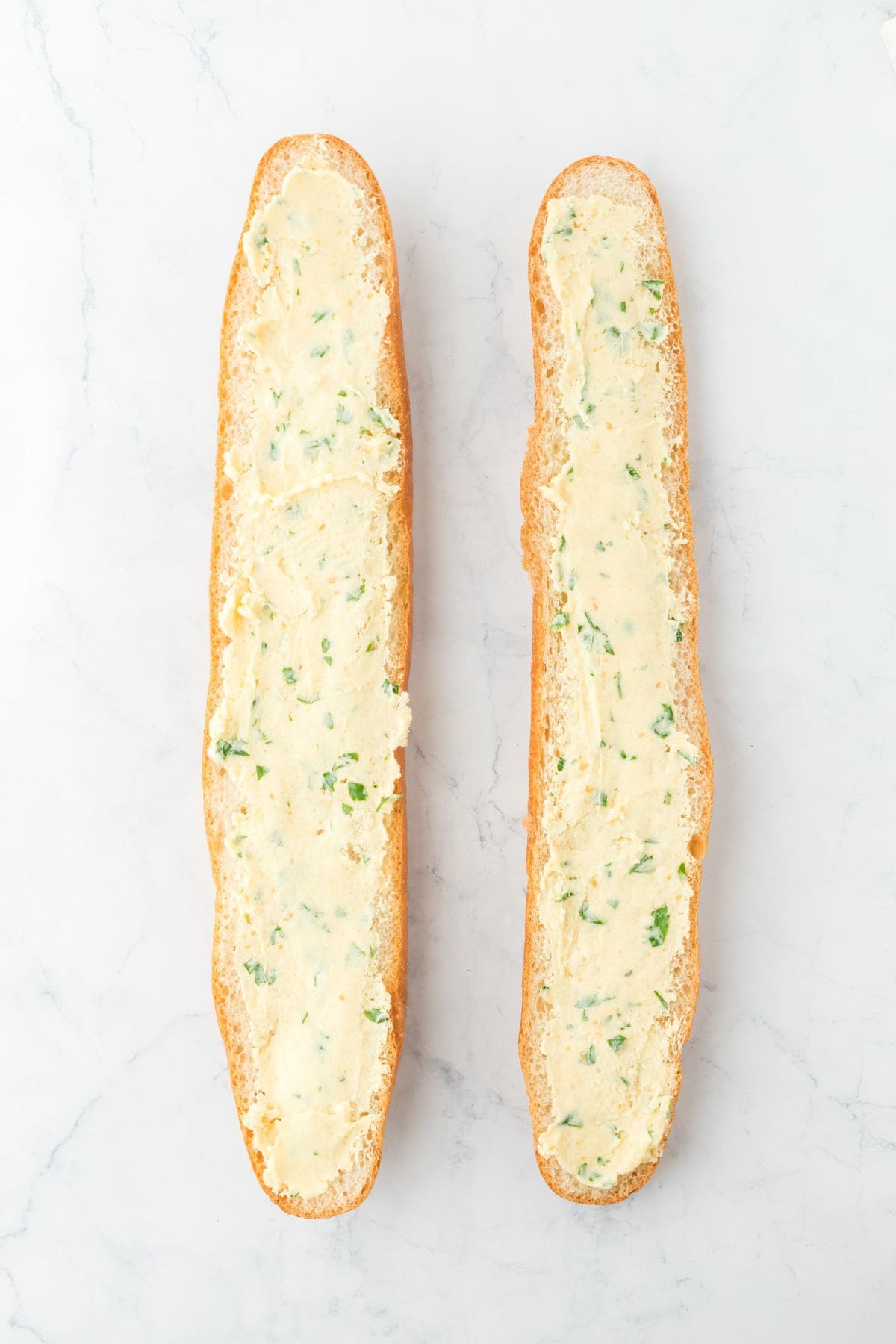 The two bread halves spread with the garlic butter mixture, ready for baking