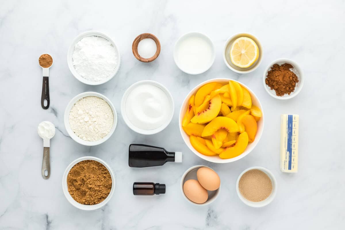 Peaches, eggs, sugar, butter, vanilla in white bowls on white background