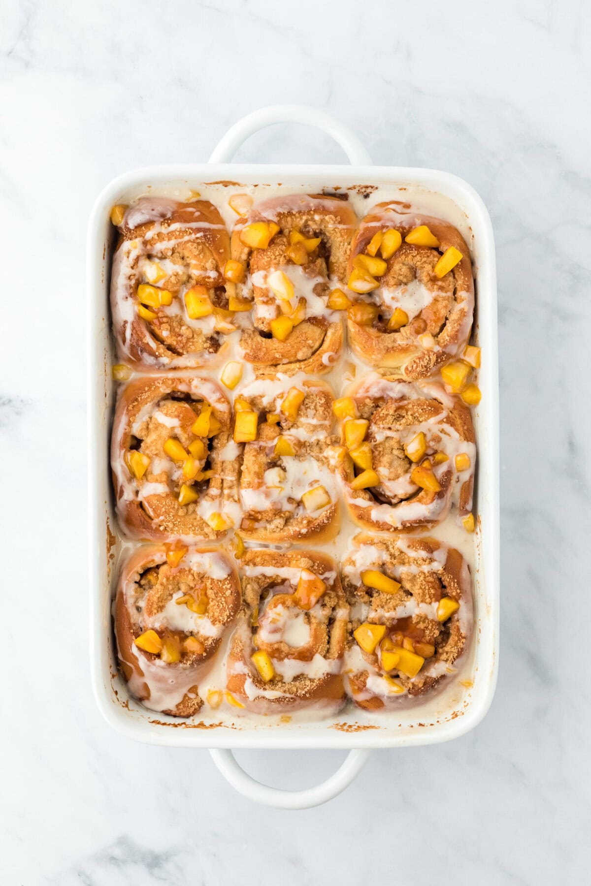 cinnamon roll peach cobbler after being baked in a white baking pan on a white background