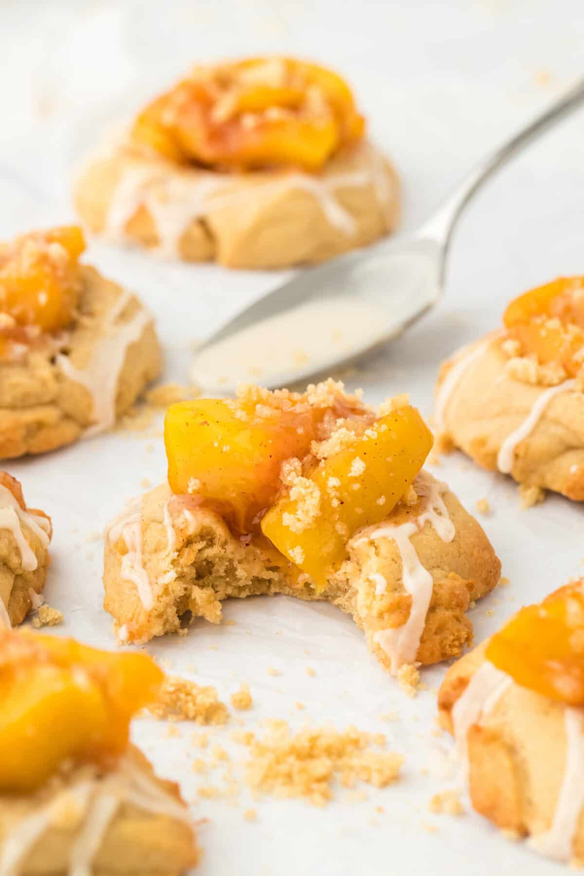 A peach cobbler cookie biten along with other peach cobbler cookies surround it on a white background