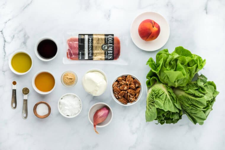 Lettuce, pecans, prosciutto, shallots, and peaches on a white background in white bowls to make a salad