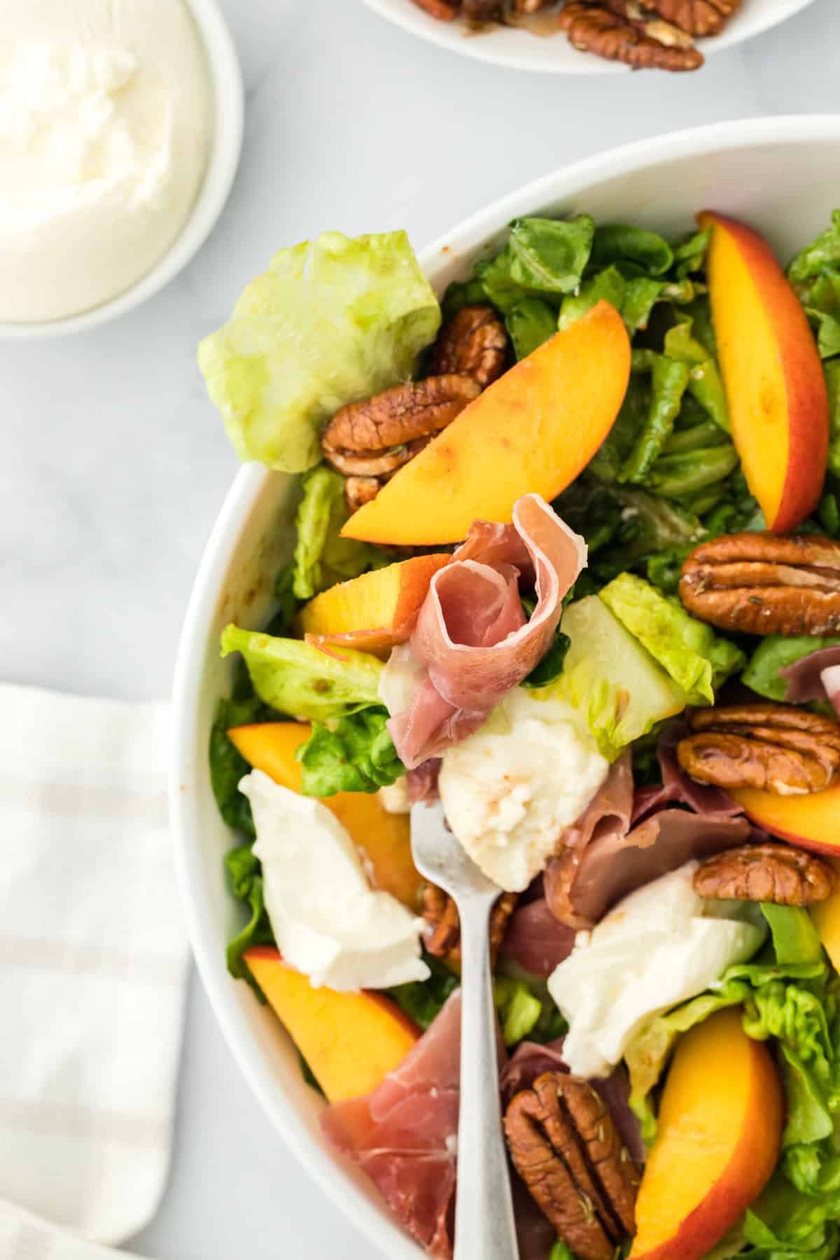 A close up of peach prosciutto salad with a fork picking some up on a white background