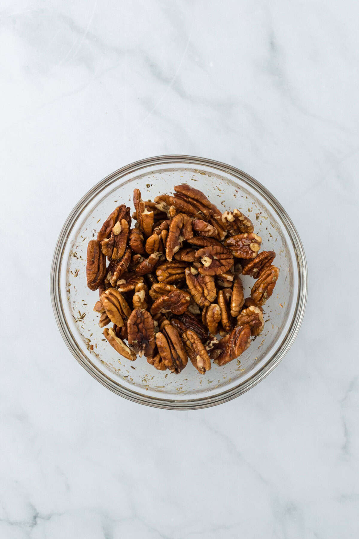 Pecans added to a candied wet mix in a clear bowl